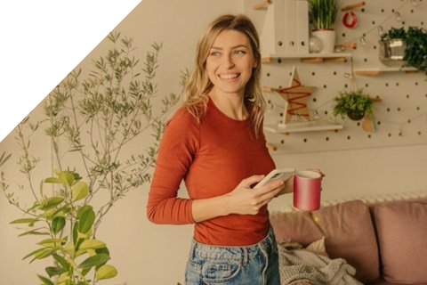 Junge Frau in ihrem Wohnzimmer mit Handy und Kaffeetasse in der Hand