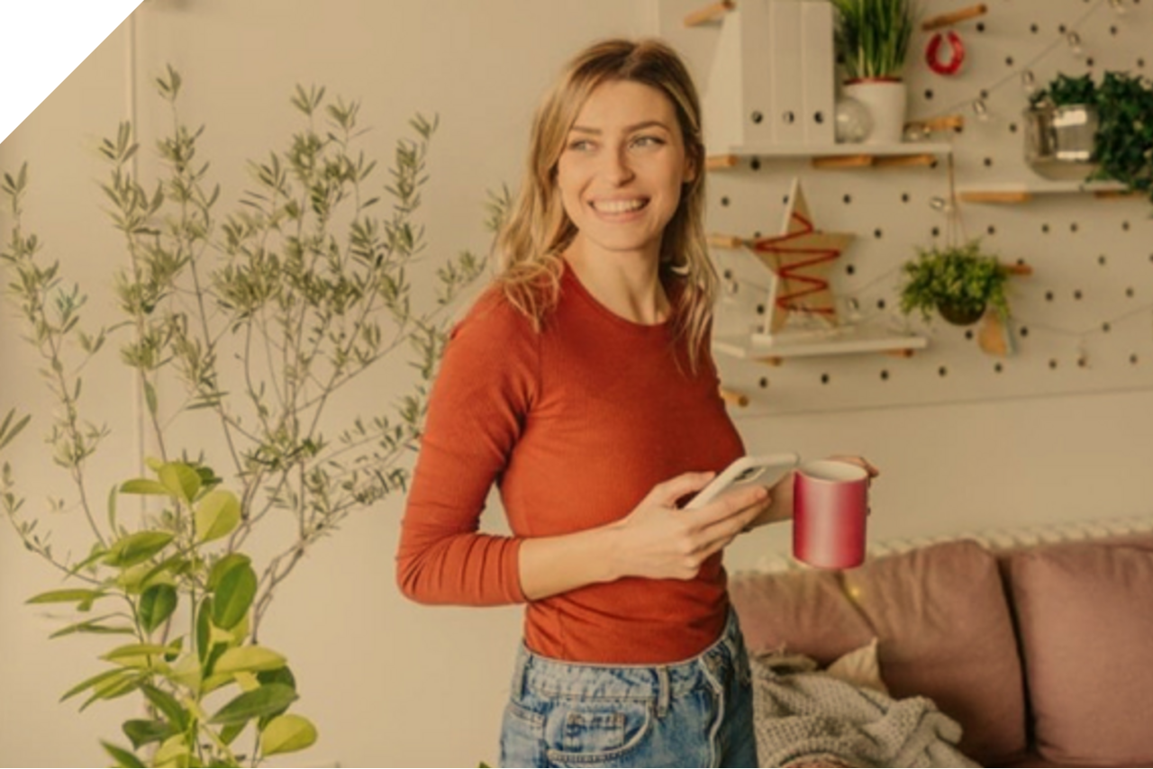 Junge Frau in ihrem Wohnzimmer mit Handy und Kaffeetasse in der Hand