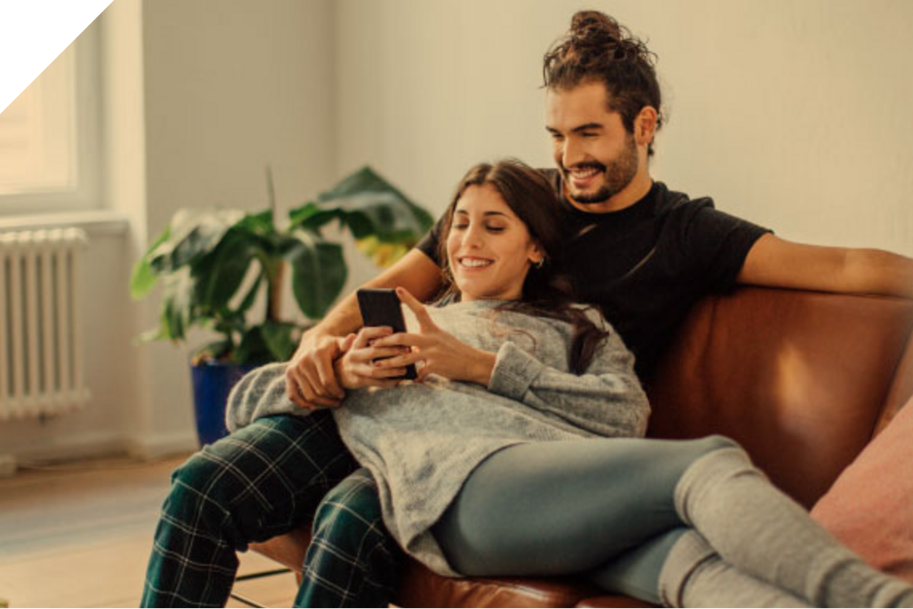 Junges Paar sitzt auf dem Sofa und schauen gemeinsam ins Handy