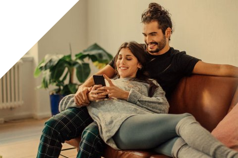 Junges Paar sitzt auf dem Sofa und schauen gemeinsam ins Handy